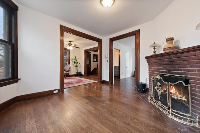 unfurnished living room featuring ceiling fan, dark hardwood / wood-style floors, and a brick fireplace