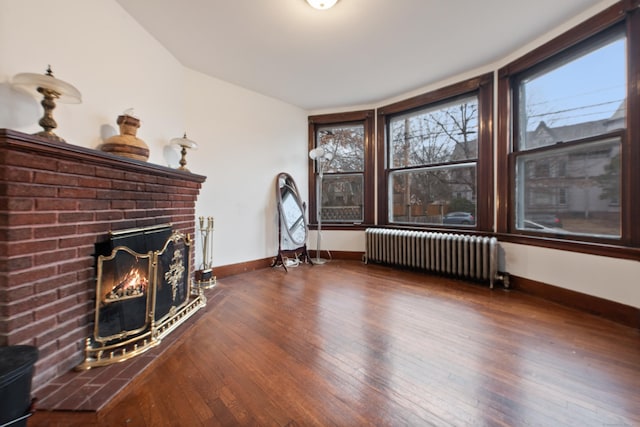 unfurnished living room featuring radiator heating unit, dark wood-type flooring, and a brick fireplace