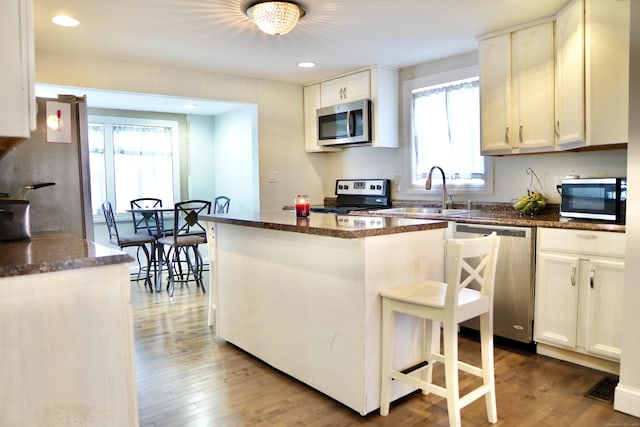 kitchen with a kitchen breakfast bar, stainless steel appliances, white cabinetry, and sink