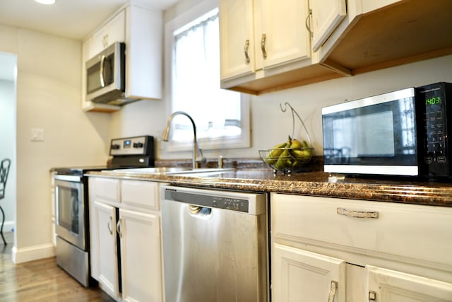 kitchen with appliances with stainless steel finishes, light wood-type flooring, dark stone counters, sink, and white cabinets