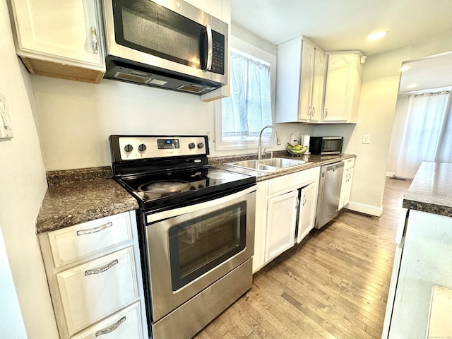 kitchen with white cabinetry, sink, stainless steel appliances, dark stone counters, and light wood-type flooring