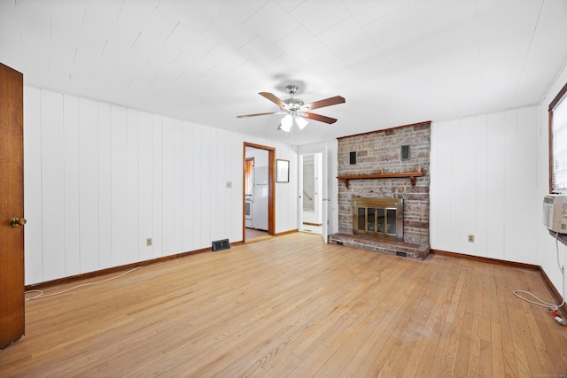 unfurnished living room with wood walls, ceiling fan, light hardwood / wood-style floors, and a fireplace