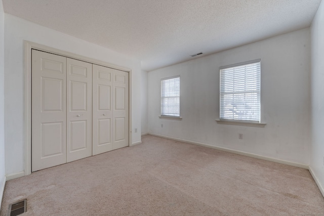 unfurnished bedroom with a textured ceiling, light carpet, and a closet