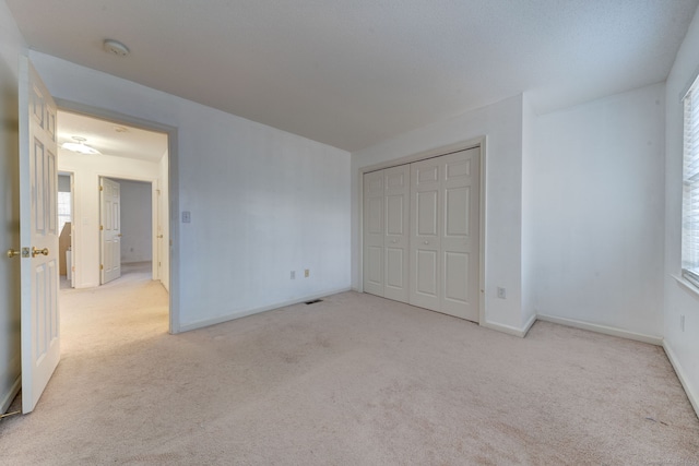 unfurnished bedroom with light colored carpet and a closet