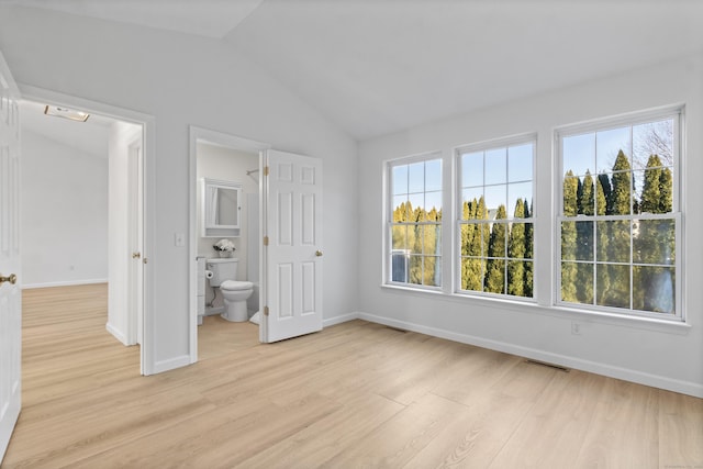 unfurnished bedroom featuring vaulted ceiling, multiple windows, light hardwood / wood-style floors, and ensuite bath