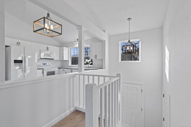 stairway with wood-type flooring, a notable chandelier, a wealth of natural light, and vaulted ceiling