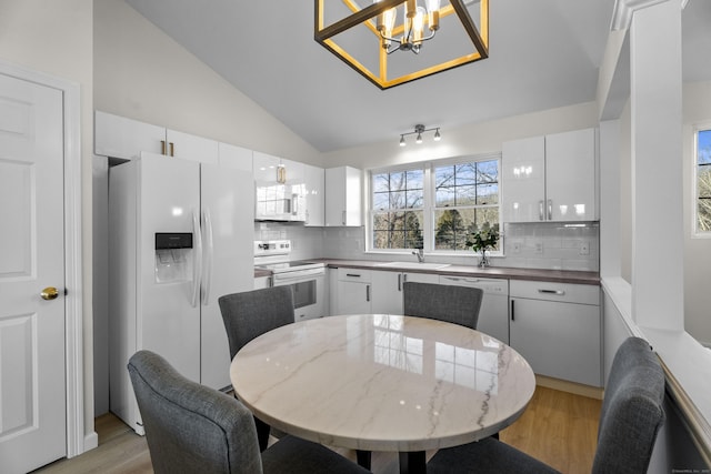 dining room featuring high vaulted ceiling, sink, light hardwood / wood-style flooring, and an inviting chandelier