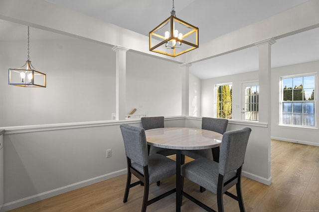 dining area with vaulted ceiling, a notable chandelier, decorative columns, and light hardwood / wood-style flooring