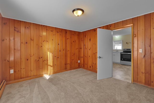 carpeted spare room featuring baseboard heating, wooden walls, and sink