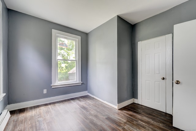 unfurnished room with dark hardwood / wood-style flooring and a baseboard heating unit