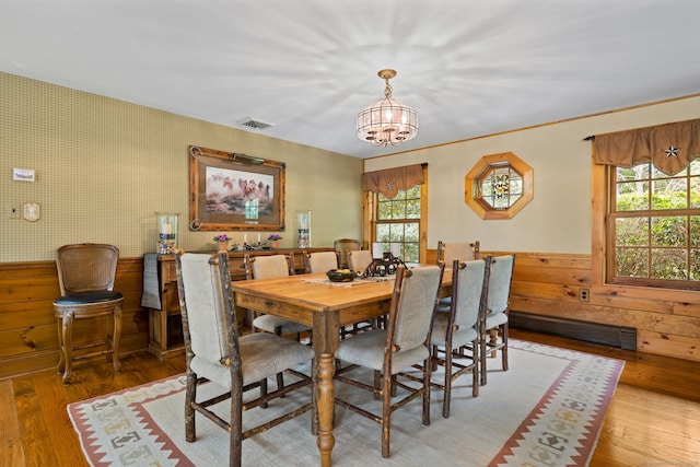 dining room with hardwood / wood-style flooring, a baseboard heating unit, wood walls, and an inviting chandelier