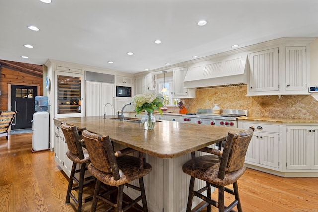 kitchen with white cabinetry, premium range hood, a kitchen island with sink, and black microwave