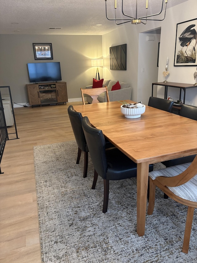 dining space featuring light wood-type flooring, a textured ceiling, and a chandelier