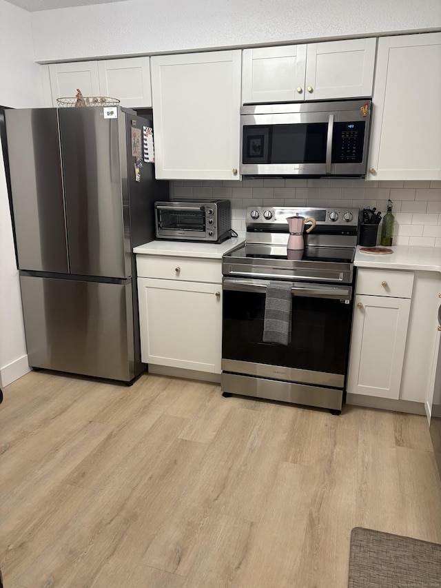 kitchen with white cabinets, light wood-type flooring, stainless steel appliances, and backsplash