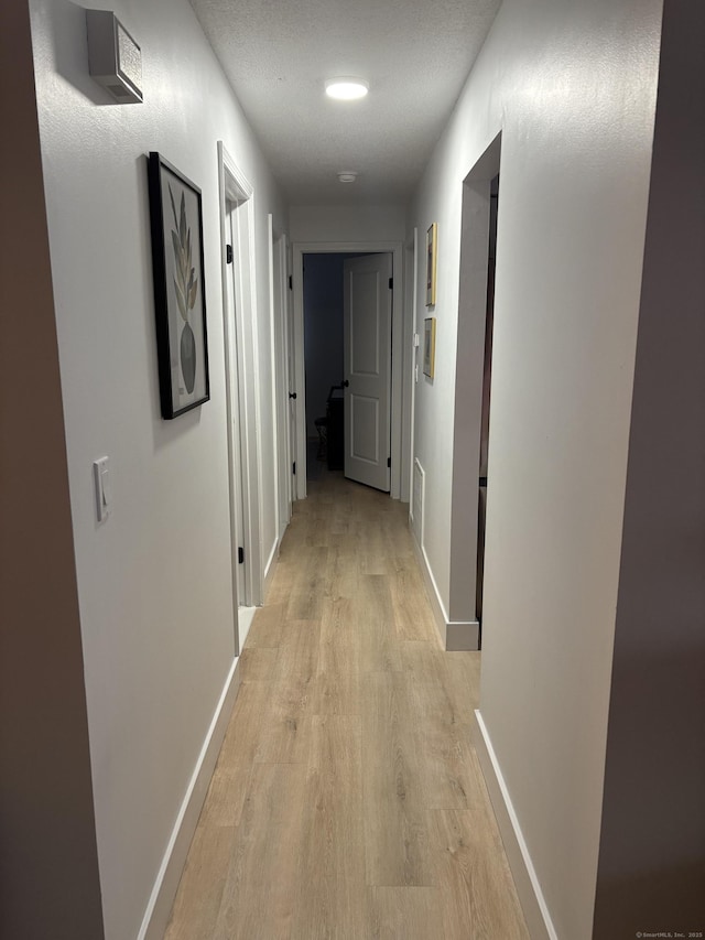 hallway with a textured ceiling and light hardwood / wood-style flooring