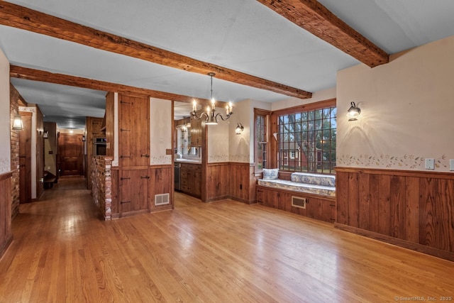 unfurnished dining area with a chandelier, beamed ceiling, light hardwood / wood-style floors, and wooden walls