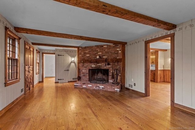 unfurnished living room featuring beamed ceiling, light hardwood / wood-style floors, a brick fireplace, and wooden walls