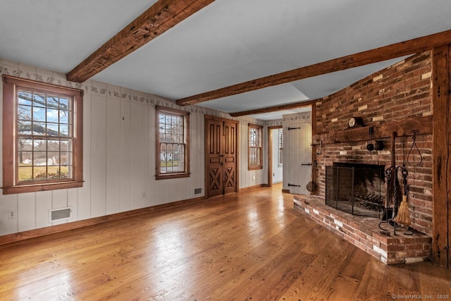 unfurnished living room with beam ceiling, wood-type flooring, and a brick fireplace