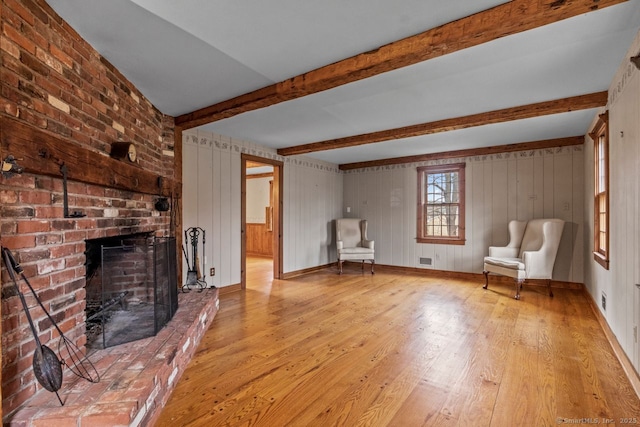 unfurnished room featuring beamed ceiling, light wood-type flooring, a fireplace, and wood walls