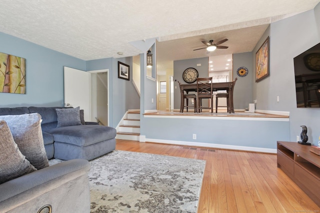 living room with a textured ceiling, light hardwood / wood-style floors, and ceiling fan