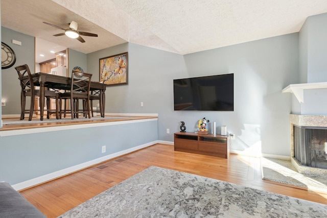 living room with vaulted ceiling, ceiling fan, a textured ceiling, a fireplace, and wood-type flooring