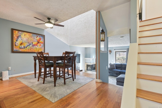 dining room featuring a textured ceiling, light wood-type flooring, ceiling fan, and lofted ceiling