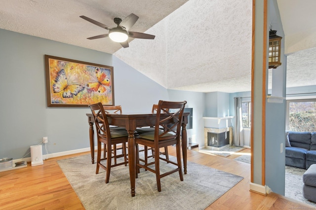 dining space featuring a fireplace, ceiling fan, hardwood / wood-style floors, and vaulted ceiling