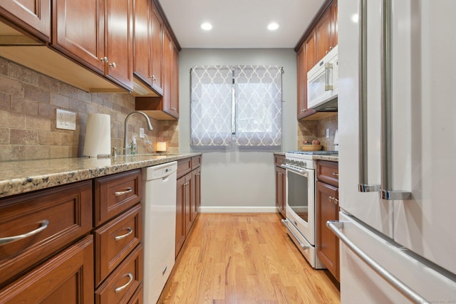 kitchen with light stone countertops, sink, light hardwood / wood-style flooring, backsplash, and white appliances