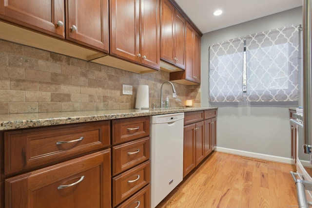 kitchen featuring white dishwasher, sink, light hardwood / wood-style flooring, decorative backsplash, and light stone counters