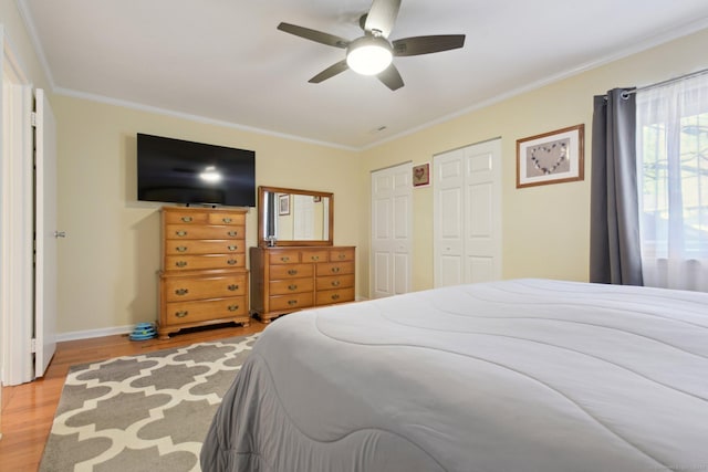 bedroom featuring multiple closets, ceiling fan, light hardwood / wood-style floors, and ornamental molding