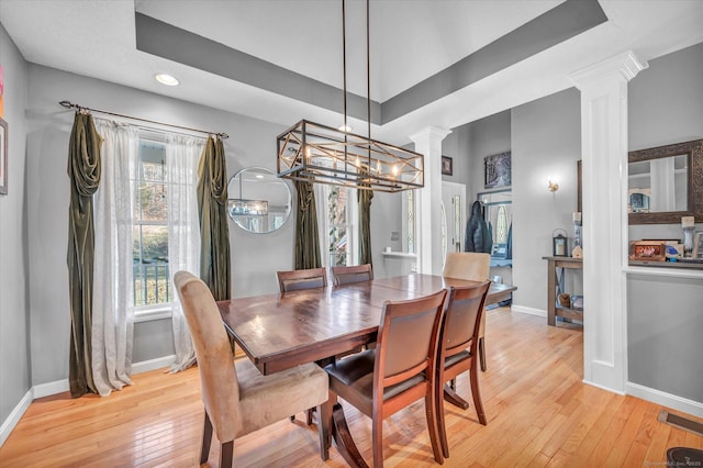 dining space featuring a tray ceiling, ornate columns, light hardwood / wood-style flooring, and an inviting chandelier