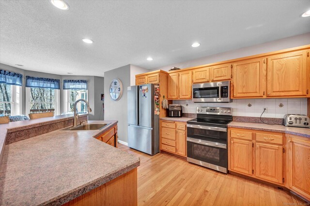 kitchen featuring decorative backsplash, light wood-type flooring, a textured ceiling, stainless steel appliances, and sink