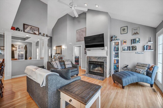 living room featuring high vaulted ceiling, a high end fireplace, hardwood / wood-style flooring, ceiling fan, and decorative columns