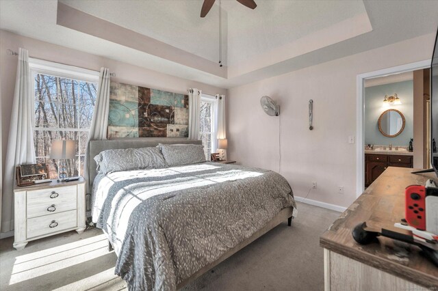 carpeted bedroom with ceiling fan, a raised ceiling, sink, and ensuite bath