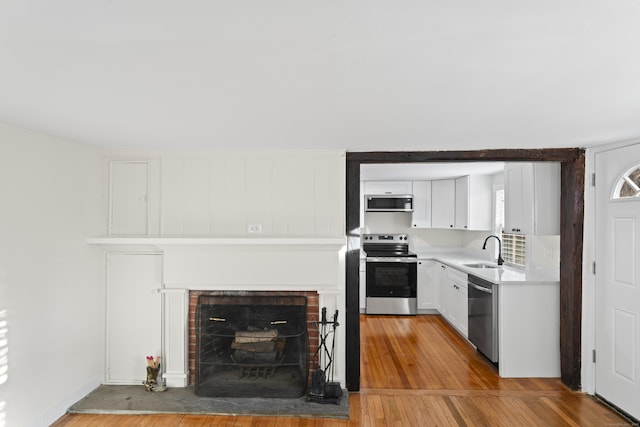 kitchen with a fireplace, sink, white cabinets, and appliances with stainless steel finishes