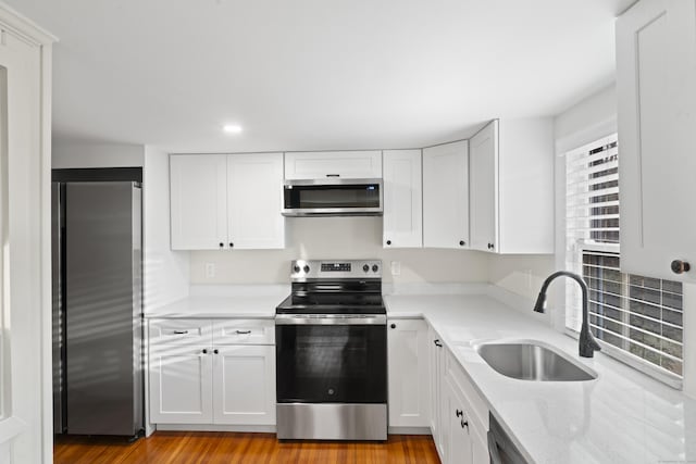 kitchen with appliances with stainless steel finishes, light hardwood / wood-style flooring, white cabinetry, and sink