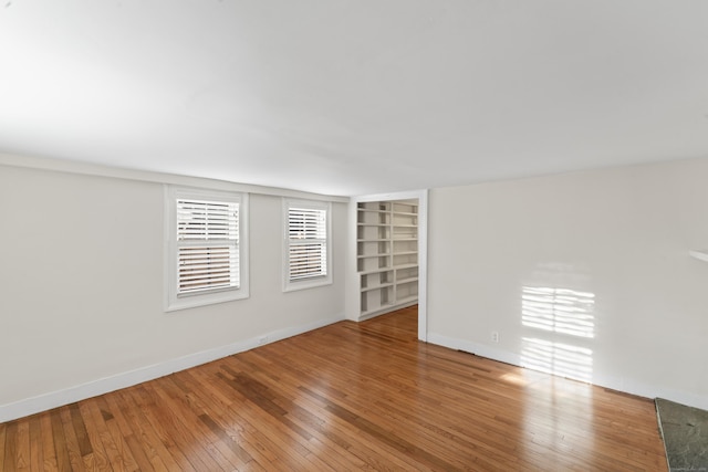 unfurnished room featuring built in shelves and hardwood / wood-style floors