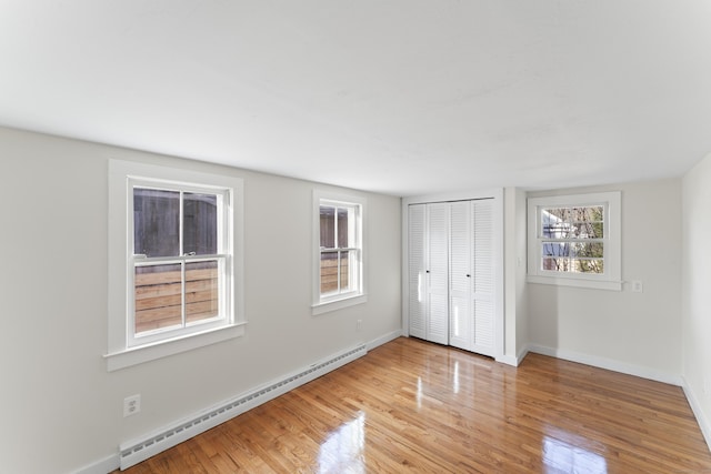 unfurnished bedroom featuring light hardwood / wood-style floors, a closet, and a baseboard heating unit