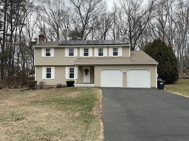 view of front facade featuring a front lawn, a garage, and solar panels