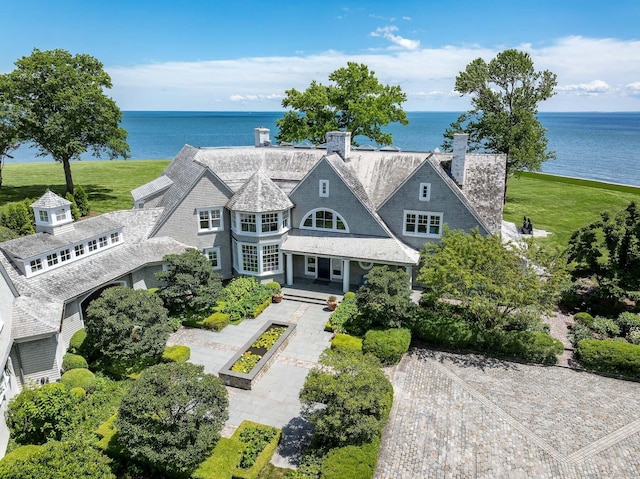 view of front facade featuring a chimney, a front lawn, decorative driveway, and a water view