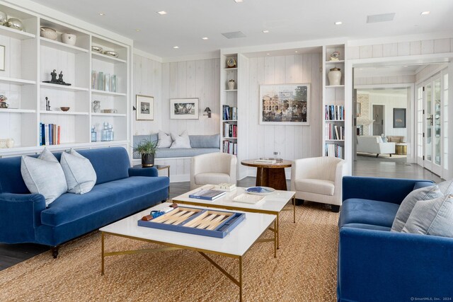 living room featuring built in shelves, wood walls, wood-type flooring, and french doors