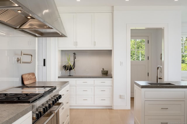 kitchen featuring stovetop, white cabinetry, a sink, and exhaust hood