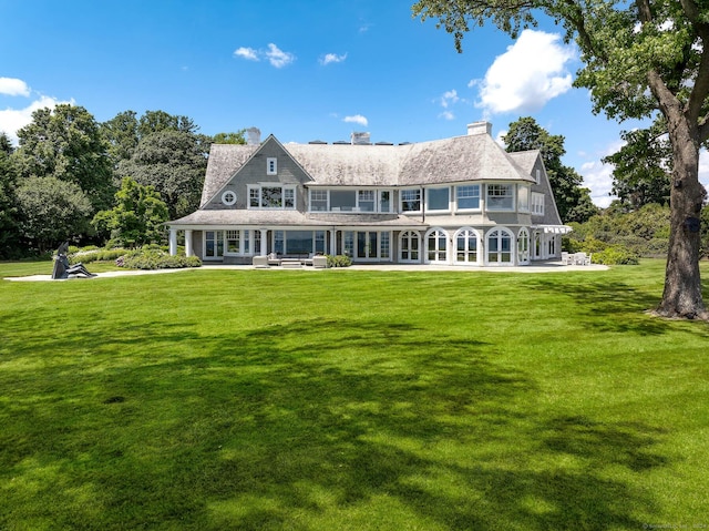rear view of property featuring a patio area, a yard, a chimney, and a balcony