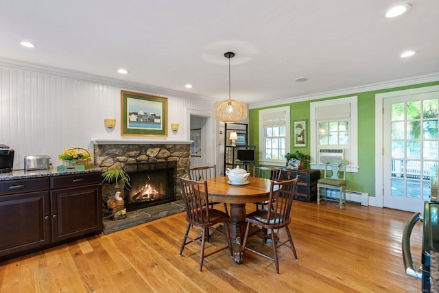 dining area featuring crown molding, a baseboard radiator, a stone fireplace, and light hardwood / wood-style flooring