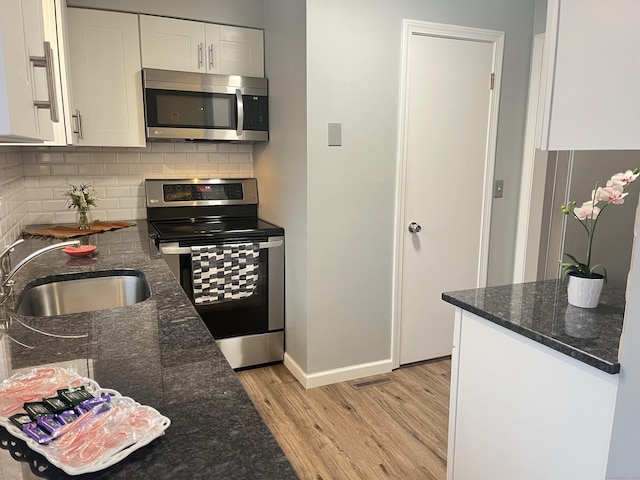 kitchen featuring white cabinetry, sink, stainless steel appliances, dark stone countertops, and light hardwood / wood-style floors