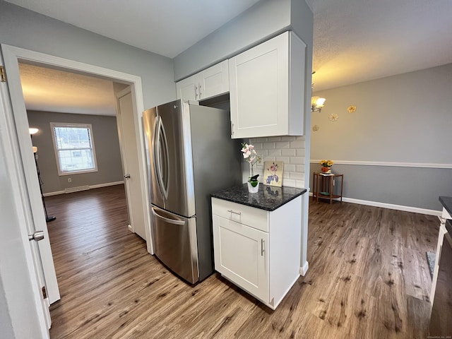 kitchen featuring light wood-type flooring, backsplash, dark stone countertops, white cabinetry, and stainless steel refrigerator