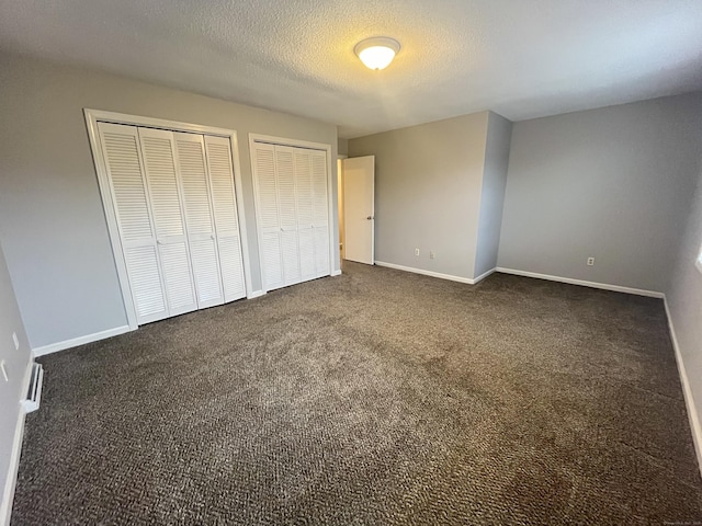 unfurnished bedroom with dark colored carpet, a textured ceiling, and multiple closets