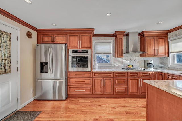 kitchen featuring appliances with stainless steel finishes, light hardwood / wood-style floors, crown molding, and wall chimney exhaust hood