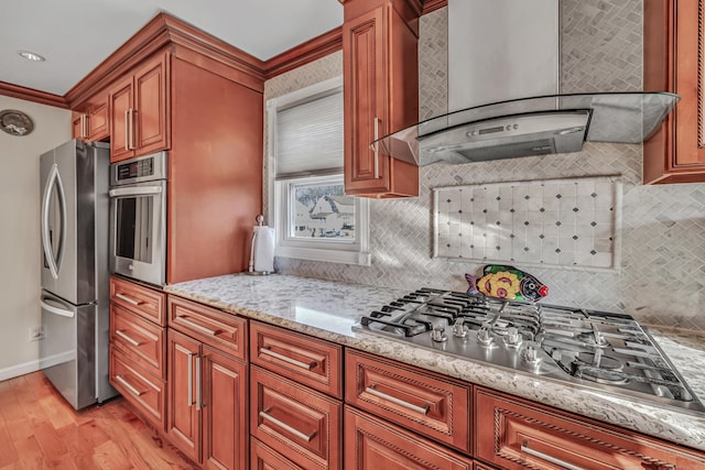 kitchen with light stone counters, stainless steel appliances, crown molding, wall chimney range hood, and light hardwood / wood-style floors