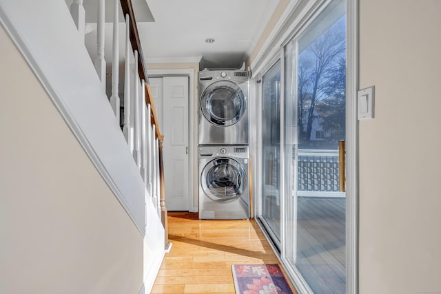 laundry room featuring light hardwood / wood-style floors, stacked washing maching and dryer, and crown molding